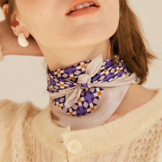 Silk bandana scarf tied around neck featuring purple, pink and orange geometric mosaic pattern, paired with cream sweater and minimalist earring