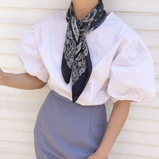 Navy blue silk bandana scarf with white paisley pattern styled around neck with white puff-sleeve blouse and gray skirt