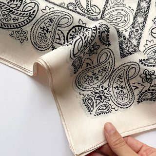 Light beige silk scarf with black paisley pattern, featuring elegant floral designs and intricate detailing, displayed folded to show natural sheen and texture