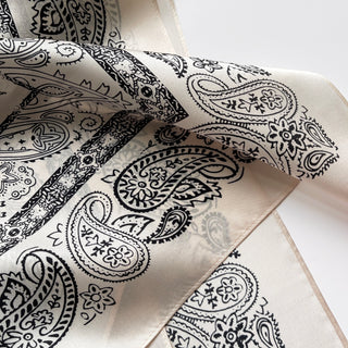 Light beige silk scarf with intricate black paisley pattern design, showing luxurious silky texture and elegant traditional motifs