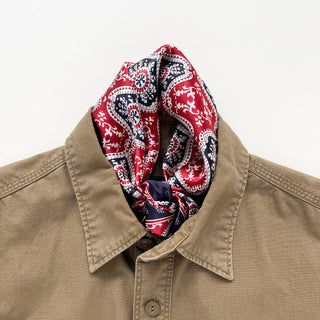 Red and navy silk bandana with geometric floral pattern styled around neck of tan button-up shirt, showcasing elegant paisley design