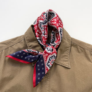 Red and navy silk bandana tied stylishly around collar of tan jacket, showcasing intricate geometric floral pattern with white accents