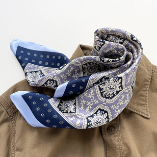 Elegant silk bandana scarf in navy and lavender with ornate floral geometric pattern, styled casually on a beige shirt collar