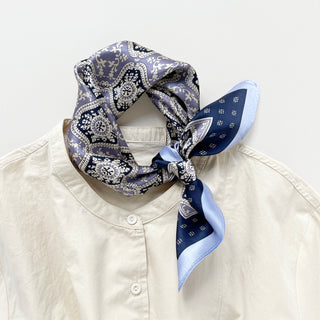 Silk bandana in navy and lavender with ornate geometric floral pattern, knotted around collar of cream shirt, showcasing luxurious sheen