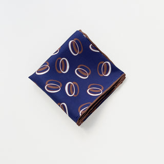 Folded indigo purple silk scarf with modern orbital pattern featuring white and brown circular designs and hand-rolled edges