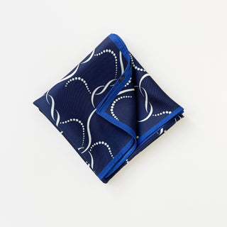 Navy blue silk scarf with white flowing geometric pattern and bright blue hand-rolled edges, folded neatly in a square shape