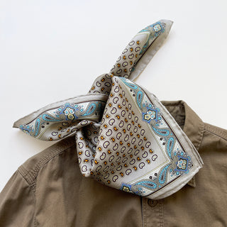 Taupe silk neckerchief with blue and gold paisley border pattern, styled on khaki shirt collar, showcasing hand-rolled edges and premium fabric