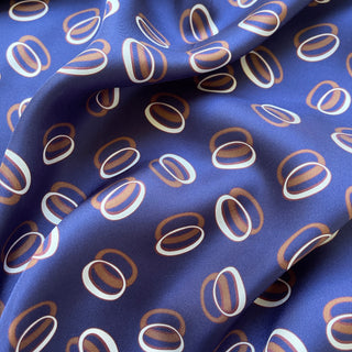 Indigo purple silk scarf with modern gold and white circular orbit pattern, showing luxurious twill fabric texture in elegant folds