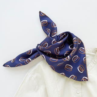 Indigo purple silk bandana scarf with brown and white circular orbit pattern, elegantly knotted on a cream collar shirt