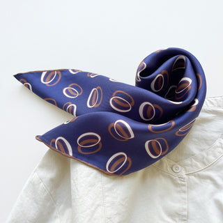 Indigo purple silk bandana scarf with modern orbit pattern featuring white and copper circular designs, elegantly draped on a white shirt collar.