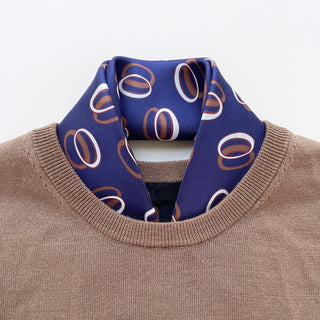Indigo purple silk scarf with modern circular orbit pattern in copper and white, styled inside the neckline of a beige sweater