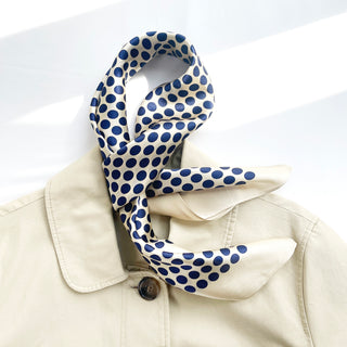 Square silk scarf with blue polka dots on cream background, draped elegantly around the collar of a light beige coat