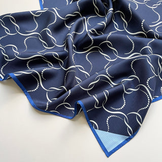 Navy silk scarf with white chain-link pattern, royal blue hand-rolled edges and light blue corner accent, displayed with elegant folds