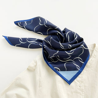 Navy blue silk scarf with white chain-link pattern, royal blue edging, and light blue corner detail, styled on white shirt.