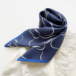 Navy blue silk scarf with white chain-link and dotted pattern, featuring royal blue border trim, elegantly draped on a white shirt.