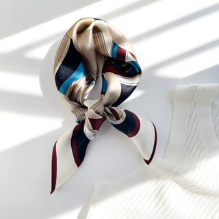 Silk Bauhaus scarf tied in a knot featuring geometric patterns in burgundy, navy, blue and cream with a lustrous sheen, displayed on white fabric