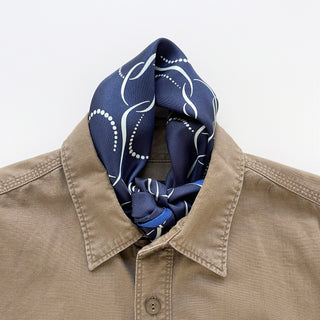 Navy blue silk scarf with white chain-link pattern and baby blue accent worn elegantly with a tan shirt, showcasing the luxurious hand-rolled finish