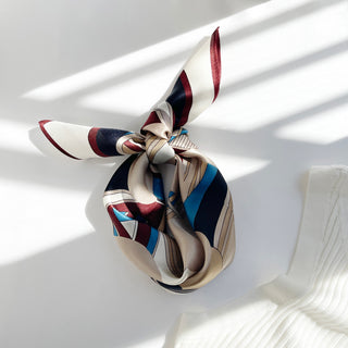 Burgundy Bauhaus silk scarf tied in a knot, featuring geometric patterns in burgundy, navy, blue, and cream with minimalist lines on white background