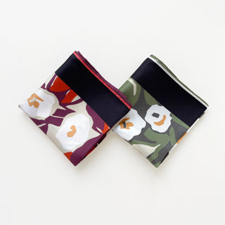 Two folded silk bandanas with floral patterns - one in burgundy purple with white blooms, one in forest green with matching design, both featuring hand-rolled edges