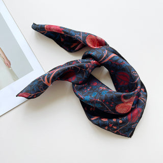 Luxury silk bandana scarf with navy blue background featuring vibrant red and pink floral pattern, displayed with hand-rolled edges showing its fine twill texture.