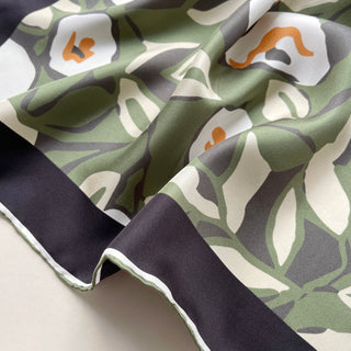 Forest green silk scarf with abstract floral pattern featuring white, gray, and orange accents, displaying hand-rolled edges and luxurious silk twill texture