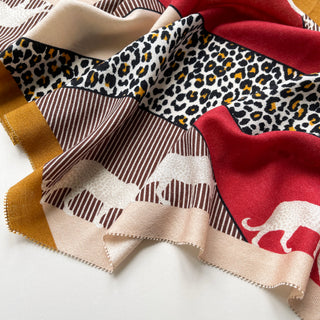 Diamond-shaped cashmere silk scarf featuring leopard print, red, beige, and mustard colors with elegant patterned sections and soft texture.