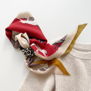 Diamond-shaped cashmere silk scarf with red, beige, and mustard tones featuring leopard print pattern, styled on cream sweater collar