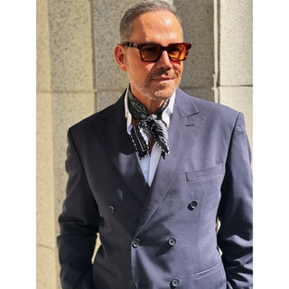 Man wearing a navy paisley patterned silk square neckerchief by LuluLane with a navy suit and sunglasses showcasing a refined sharp look.