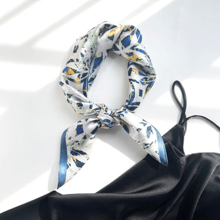 Silk bandana scarf with dusty blue and yellow floral abstract pattern, tied in a loop knot against white background with blue trim edge