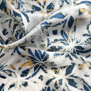 Luxurious silk scarf with artistic dusty blue and yellow floral pattern on white background, showing silky fabric texture and folds