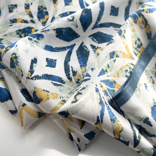 Silky white bandana scarf with artistic dusty blue and yellow floral pattern, showing luxurious fabric texture and flowing folds.