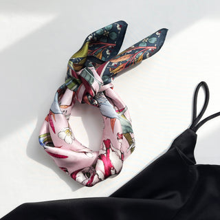 Luxurious pink silk bandana scarf with botanical floral print featuring dark green borders, displayed elegantly folded on white background