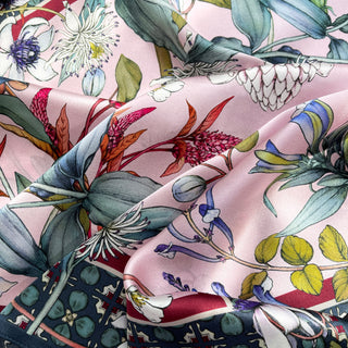 Luxury pink silk scarf with vibrant botanical print featuring blue-green leaves, vivid red flowers, and delicate white blooms on a soft pink background