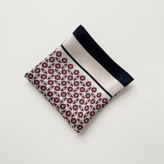Folded silk bandana scarf with red and white geometric pattern, black border, and white stripe against neutral background