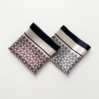 Two folded silk bandana scarves with geometric patterns - one in red and black, one in blue and white - featuring elegant borders and intricate designs.