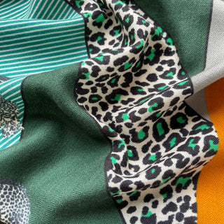 Close-up of luxury cashmere silk scarf featuring green leopard print pattern with teal striped sections and solid green fabric, showcasing soft texture