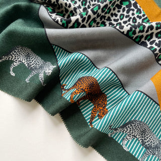Luxurious cashmere silk scarf in cool green palette with leopard print pattern, featuring orange and white leopard silhouettes on turquoise stripes with gray accents