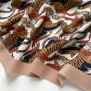 Beige brown cashmere silk scarf featuring vibrant tiger pattern with orange tigers and red ribbons on cream background, luxurious fabric texture visible.