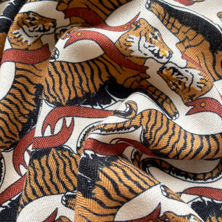 Close-up of Tiger Reverie cashmere silk scarf showing detailed pattern with orange tigers and red accents on beige background, revealing luxurious fabric texture