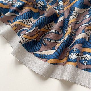 Close-up of Tiger Reverie scarf featuring blue tigers with golden accents on a mauve background, showing luxurious cashmere-silk fabric texture and pattern detail.