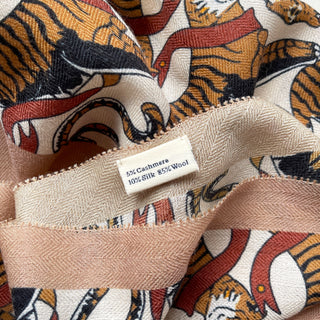 Luxury cashmere-silk scarf with tiger pattern in earth tones of beige, orange, black, and red, showing fabric composition label.
