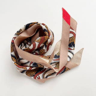 Diamond-shaped Tiger Reverie scarf in beige, brown, and red tones with tiger pattern, artfully draped to display its luxurious cashmere-silk texture and pointed ends.