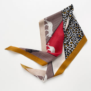 Diamond-shaped cashmere silk scarf featuring red, beige and mustard colors with leopard print pattern and subtle elephant design on white background