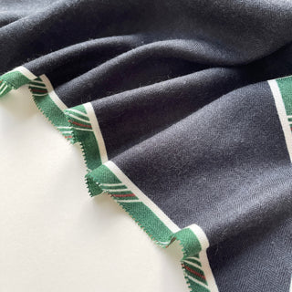 Close-up of black cashmere silk scarf with green and white plaid edge trim, showing luxurious fabric texture and elegant design.