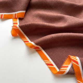 Close-up of luxurious brown cashmere silk scarf with vibrant orange plaid border, showing fine herringbone texture and elegant draping