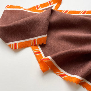 Close-up of luxury diamond-shaped cashmere silk scarf in rustic brown with vibrant orange plaid border, showing fine textile texture