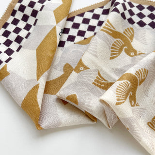Elegant beige cashmere silk scarf with Art Deco style golden bird motifs and deep brown checkered border, showing luxurious texture and drape