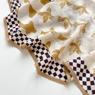 Beige silk-cashmere scarf with gold stylized birds pattern, bordered by brown and cream checkerboard trim and beige edging, shown draped elegantly