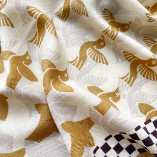 Close-up of beige cashmere silk scarf with gold stylized bird pattern and dark brown checkerboard border, showing luxurious fabric texture