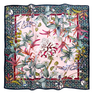 Luxurious square silk scarf with pink center featuring botanical illustrations of flowers and foliage, bordered by dark green pattern with red accent trim